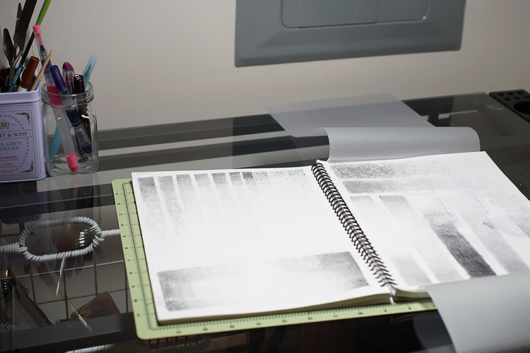 An open sketchbook ontop of a drafting table, with drawings of value practice in pencil on the pages