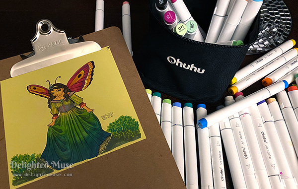 A photo of a drawing on a clipboard, with a pile of Ohuhu markers laid out on a table