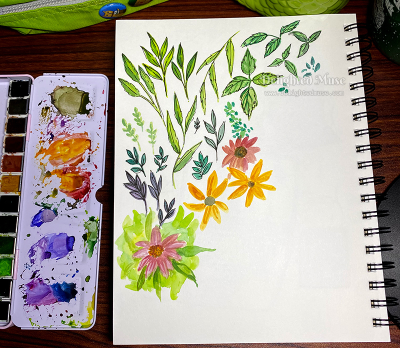 A sketchbook page with paintings of leaves and flowers. To the left is an open watercolor pan set.