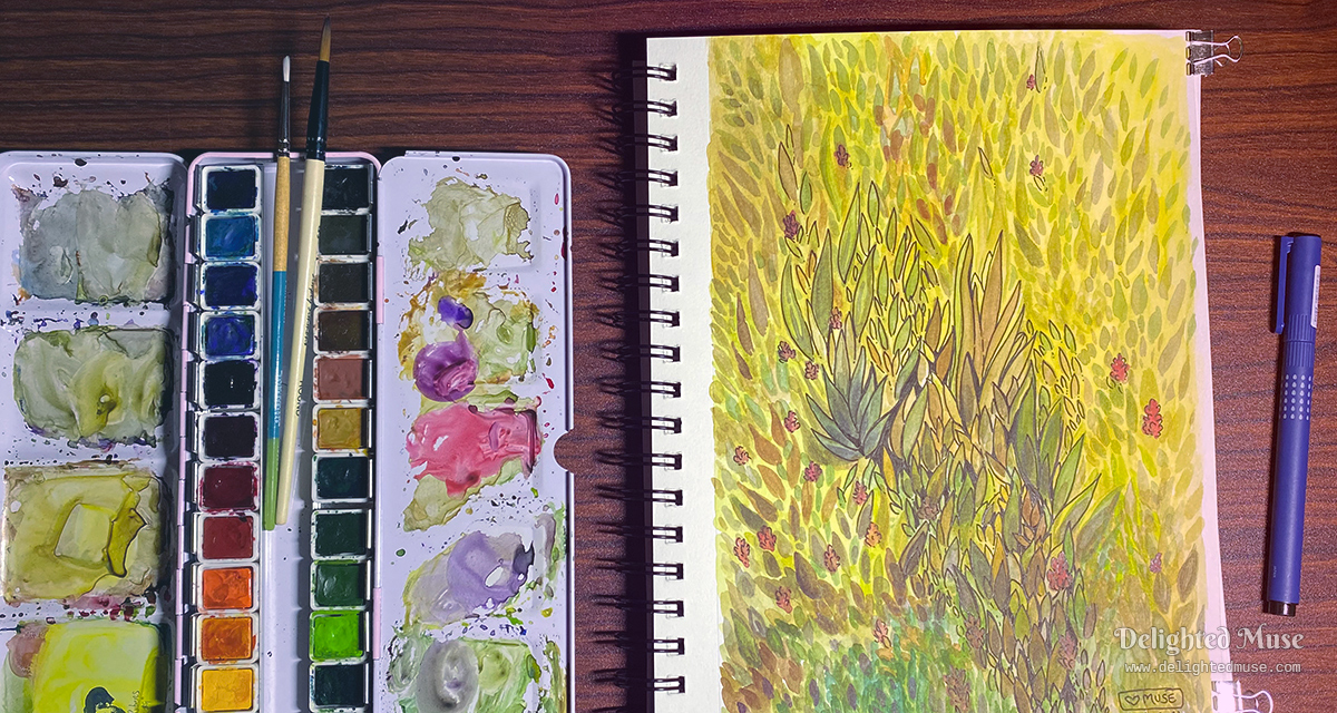 A wooden desktop showing a watercolor paint pan, brushes, a sketchbook page with an abstrack leaf pattern, and an fineliner ink pen.