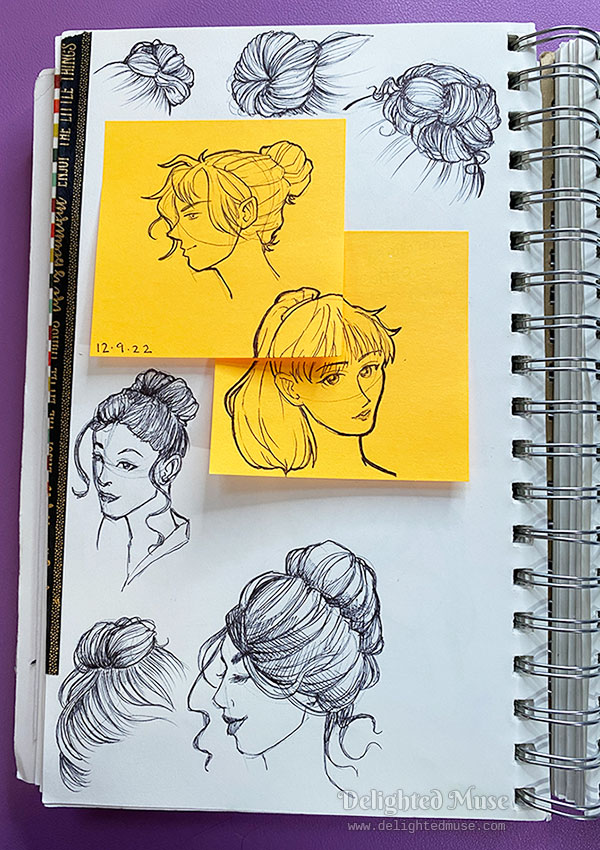 Sketchbook page of rough sketches of bun hairstyles in ball point pen, and in the middle of the page are two orange sticky notes with women wearing a bun hair style and a pony tail hairstyle.
